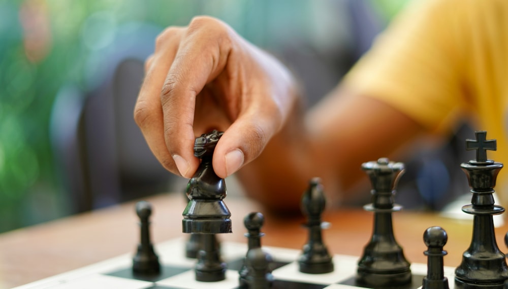 Man playing chess holding up a chess piece (knight) to make his next move.