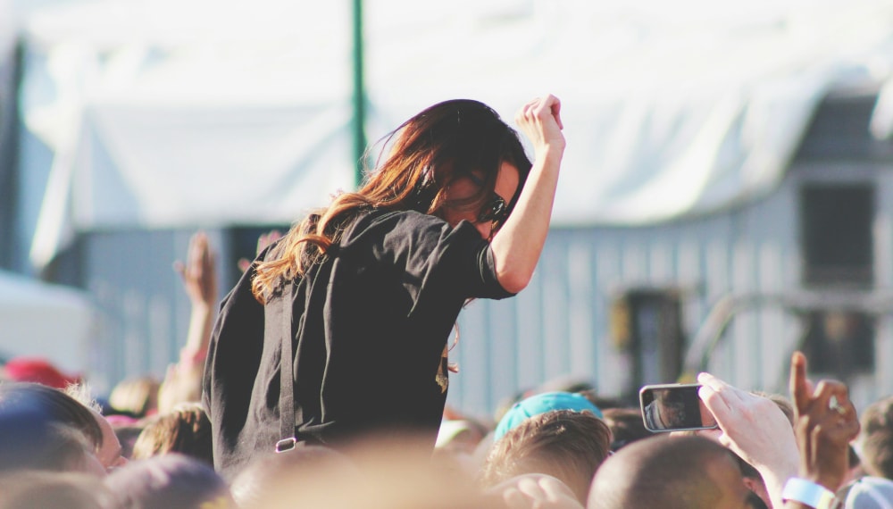 Girl sitting on the shoulders of another person inside a festival crowd enjoying herself.
