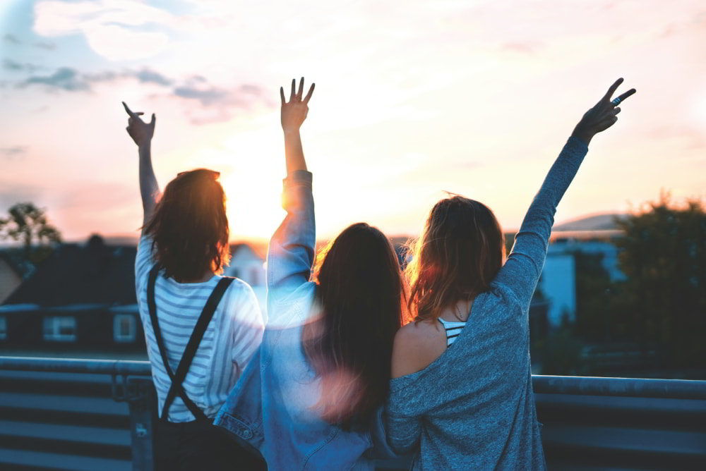 Three young adults celebrating on the roof of a building in the city.