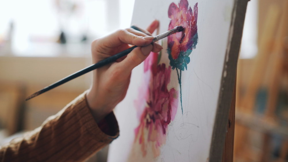 A woman's hand painting a flower on a canvas.
