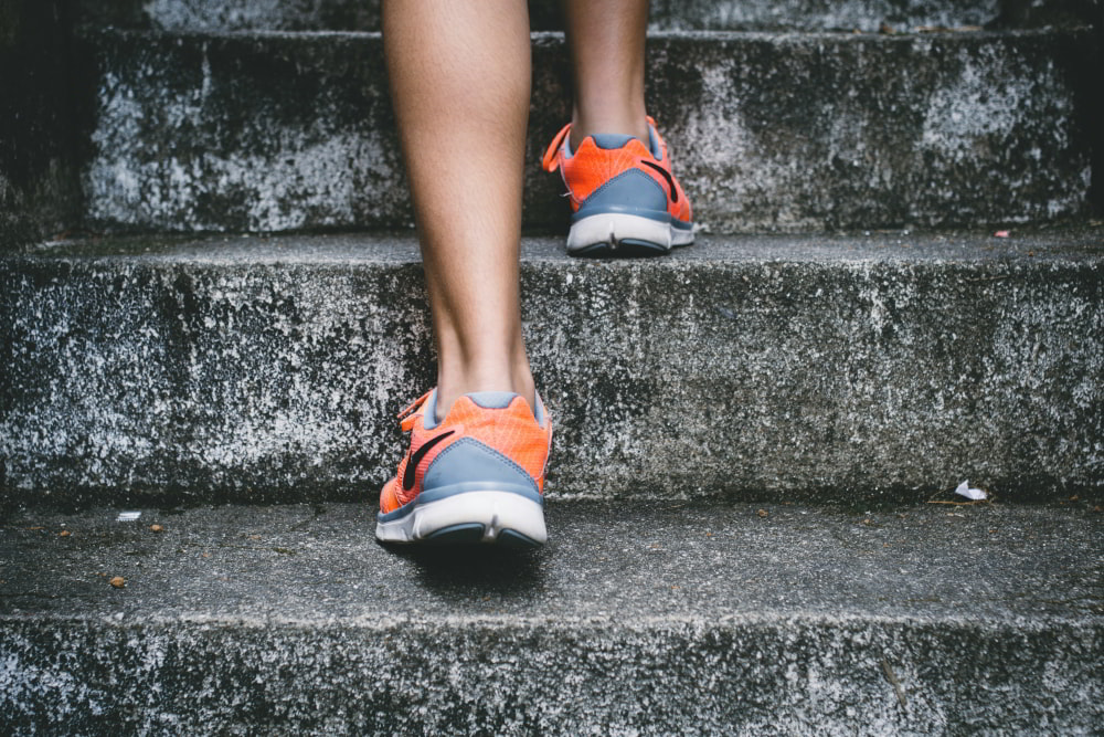 Legs of a male with running shoes on climbing concrete stairs outside.