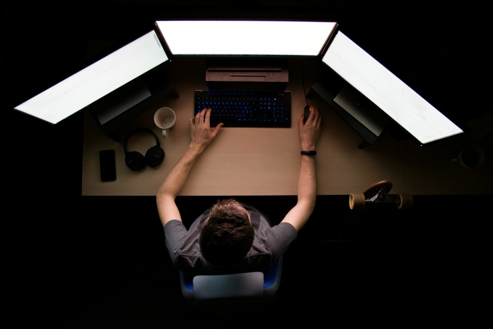 Top down image of a man behind desk with three monitors in front of him.